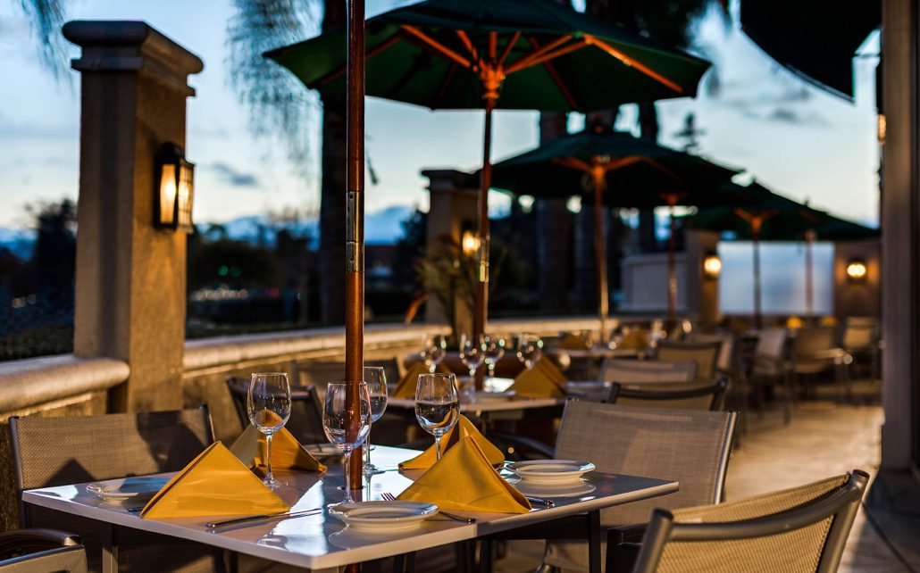 Outdoor dining patio at Hilton Santa Clara with wine glasses, yellow napkins, and umbrellas at sunset