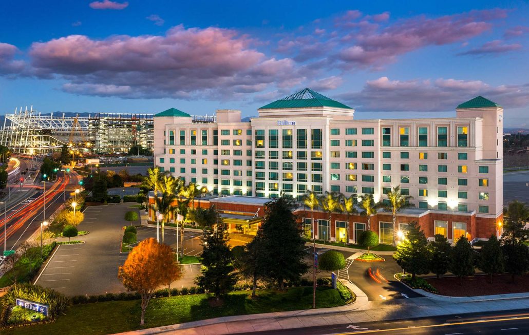 Exterior view of Hilton Santa Clara at dusk with Levi’s Stadium in the background and dramatic evening sky.