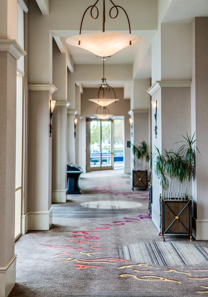 Ballroom Foyer at Hilton Santa Clara featuring carpeted corridor, tall columns, natural lighting, and lounge seating near the event spaces