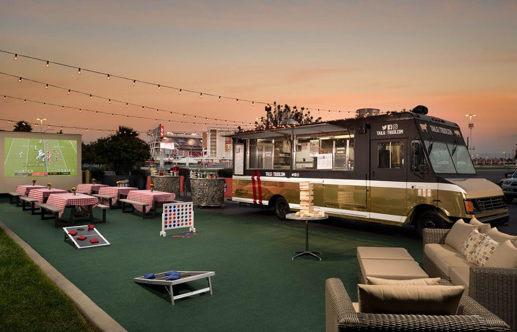 Outdoor lounge area with food truck, pink chairs, and a large screen at the Hilton Santa Clara Tailgate Zone.