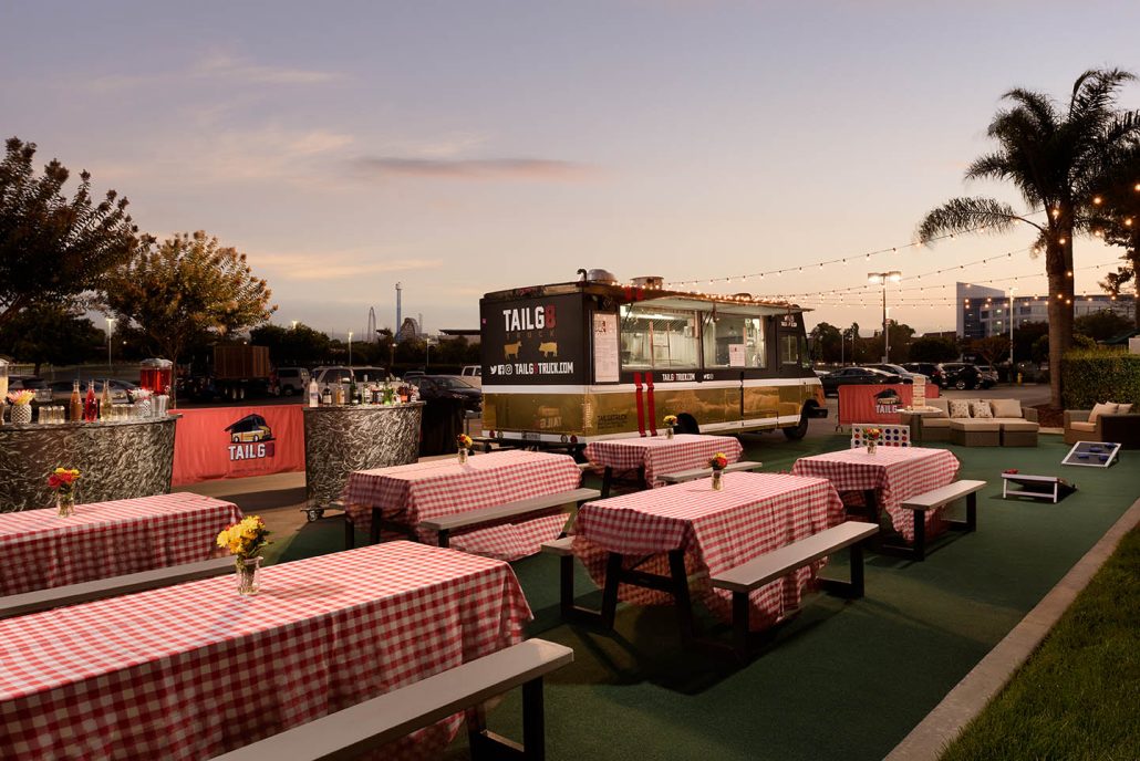 Picnic tables with red checkered tablecloths and string lights at the Hilton Santa Clara Tailgate Zone.