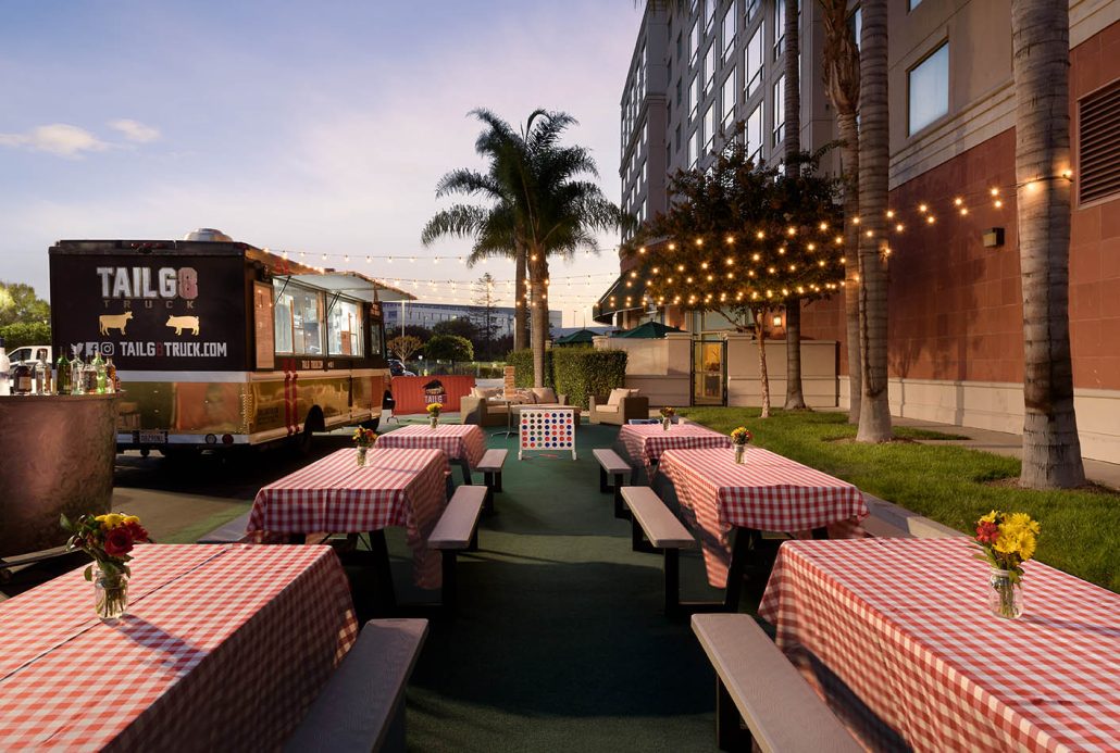 Outdoor tailgate venue at Hilton Santa Clara with picnic tables, string lights, and a food truck near Levi’s Stadium