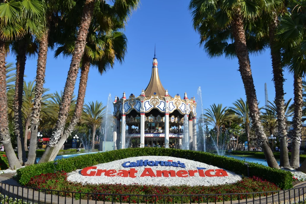 Entrance to California’s Great America with the iconic double-decker carousel and flowerbed sign surrounded by palm trees.