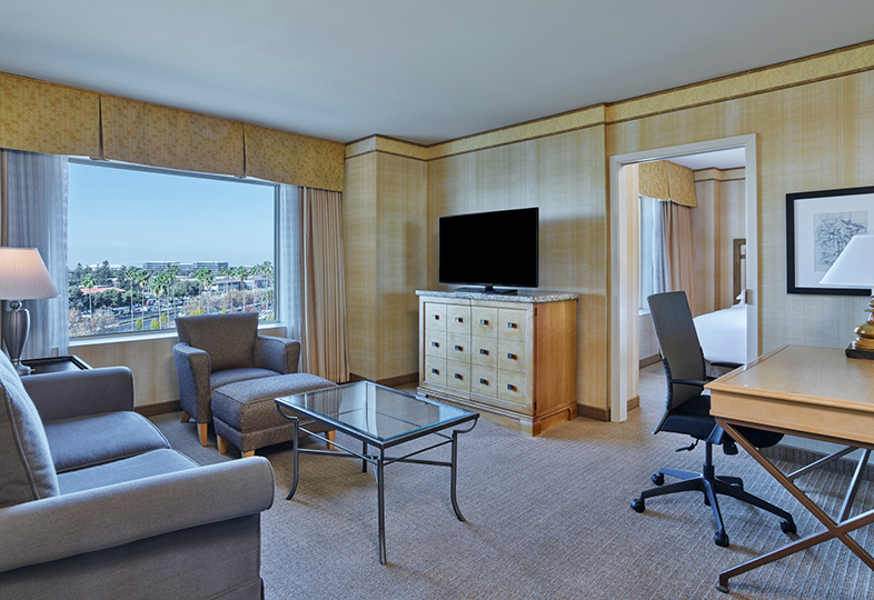 Mini suite at Hilton Santa Clara with king bed, separate seating area, and desk, featured in Santa Clara hotel suites.
